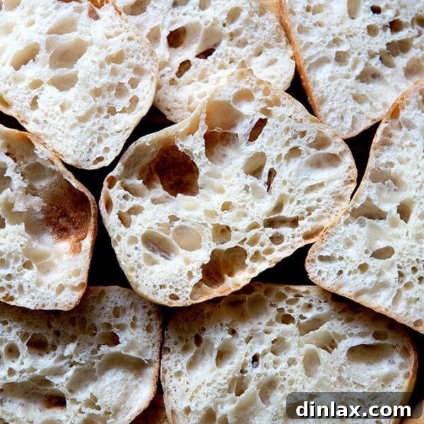 A pile of perfectly halved ciabatta rolls, showcasing their airy, open crumb texture.
