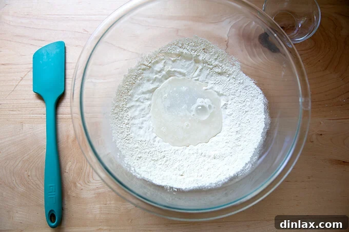 Adding water to the flour and yeast mixture in a clear glass bowl.