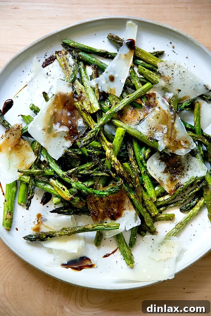Effortless Balsamic Parmesan Roasted Asparagus 13 Close-up of a serving of roasted asparagus with balsamic glaze and shaved Parmesan on a white plate, highlighting the delicious texture and toppings.