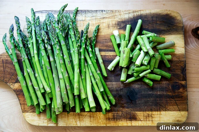 Effortless Balsamic Parmesan Roasted Asparagus 4 Asparagus spears laid out on a wooden cutting board, with the tough woody ends snapped off, ready for further preparation.