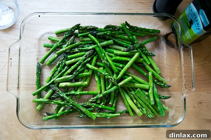 Effortless Balsamic Parmesan Roasted Asparagus 6 Raw asparagus spears in a baking dish, seasoned with salt and pepper and drizzled with olive oil, before being placed in the oven.