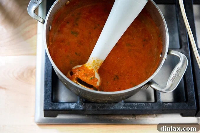 Pantry-Perfect Tomato Sauce in Minutes 10 A pot of homemade tomato sauce simmering stovetop with an immersion blender inside.