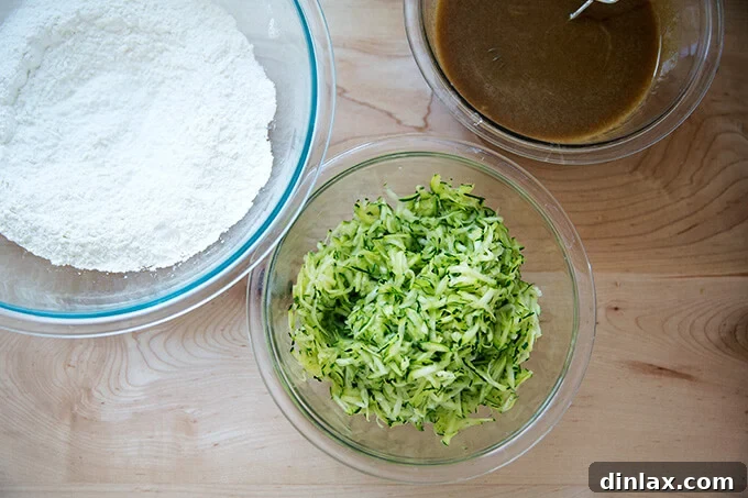Decadently Moist Zucchini Bread Bliss 5 Three separate bowls on a countertop: one containing dry ingredients, one with wet ingredients, and a third with finely grated zucchini, illustrating the prepared components for zucchini bread.