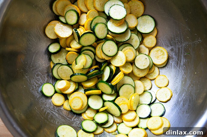 Sliced summer squash and zucchini in a large bowl, glistening with olive oil, salt, and pepper.