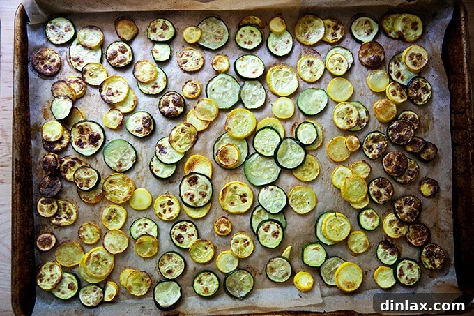 Roasted zucchini slices spread out evenly on a large sheet pan, turning golden brown.