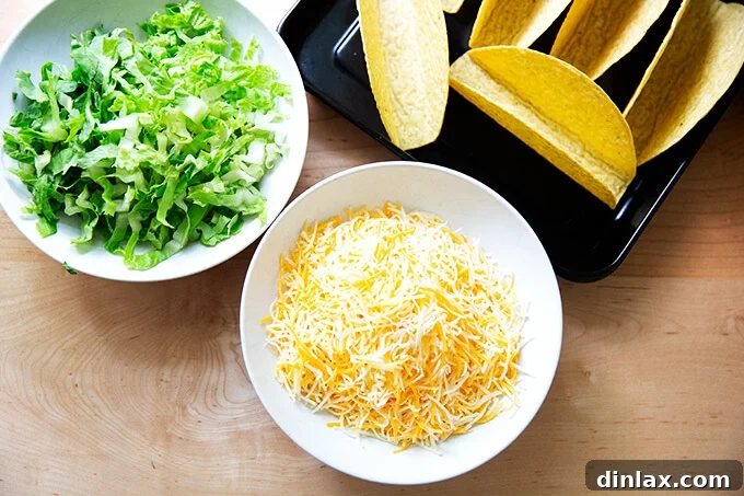 Separate bowls of shredded cheese and crisp shredded lettuce, along with hard taco shells neatly arranged on a baking sheet, all prepped for an efficient taco night assembly.