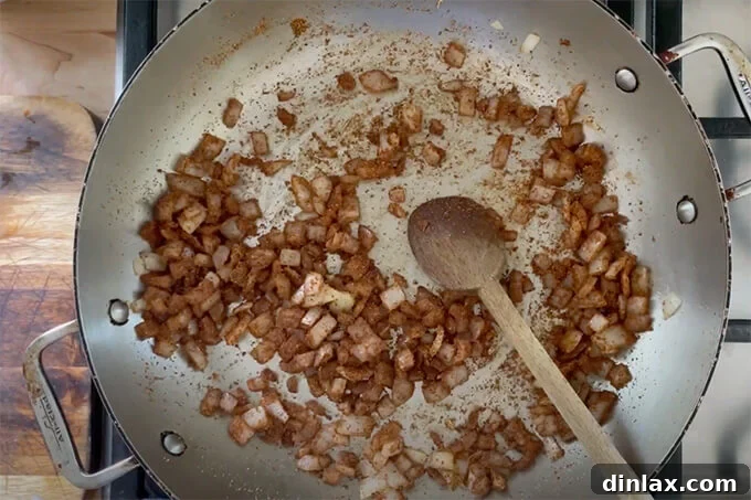 A sauté pan holding translucent diced onions and an opened packet of taco spices, releasing their enticing aromas as they cook.