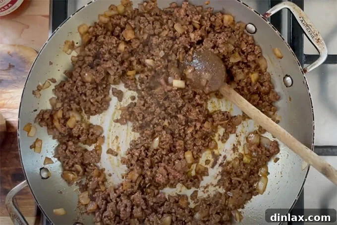 Ground beef cooking in a sauté pan alongside the fragrant onions and taco seasoning, browning evenly as it's stirred.