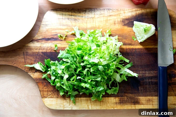 A crisp head of Romaine lettuce, freshly shredded on a cutting board, prepared as a light and refreshing topping for tacos.