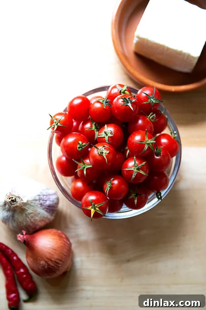 Warm Feta & Burst Tomato Bake 3 A bowl of cherry tomatoes aside a plate of feta and a head of garlic, shallots, and chilies.