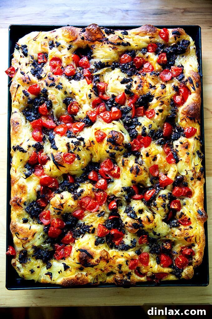 A large sheet pan holding a freshly baked Pissaladière, boasting a golden crust and glistening, aromatic toppings.