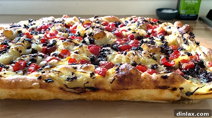 Baked Pissaladière, viewed from the side, resting beautifully on a wooden board, highlighting its layers.