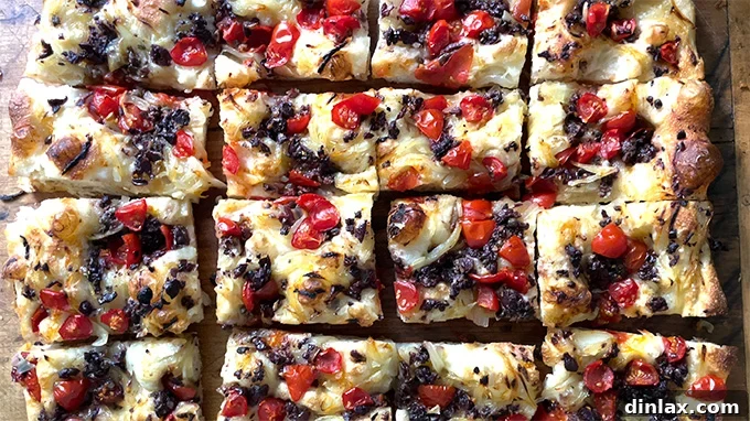 Baked Pissaladière on a board, partially cut into squares, showcasing its appetizing appearance.
