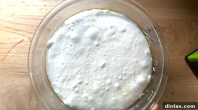 Sourdough focaccia dough undergoing bulk fermentation in a large glass bowl, showing its readiness for the next stage of preparation.