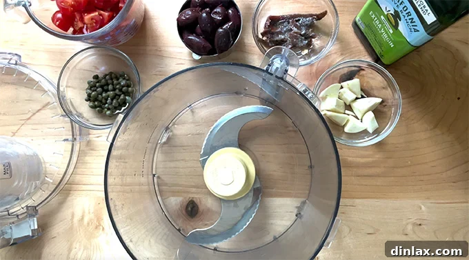 A selection of essential ingredients laid out for making the anchovy purée, including garlic, anchovies, olives, capers, and olive oil.