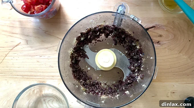 Olive and anchovy purée being created in a food processor, displaying its desirable coarse and textured consistency.