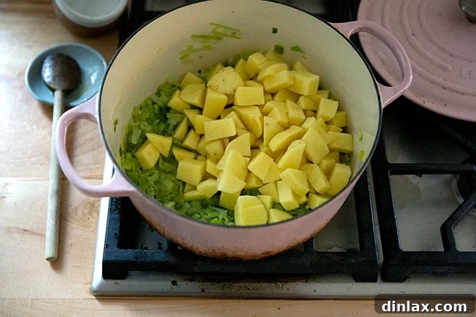 A large soup pot containing sautéed leeks and diced potatoes.