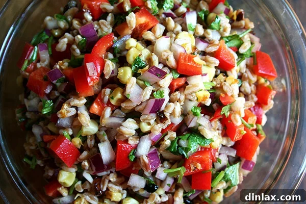 A colorful serving of roasted corn, onion, red pepper, and farro salad, ready to be enjoyed.