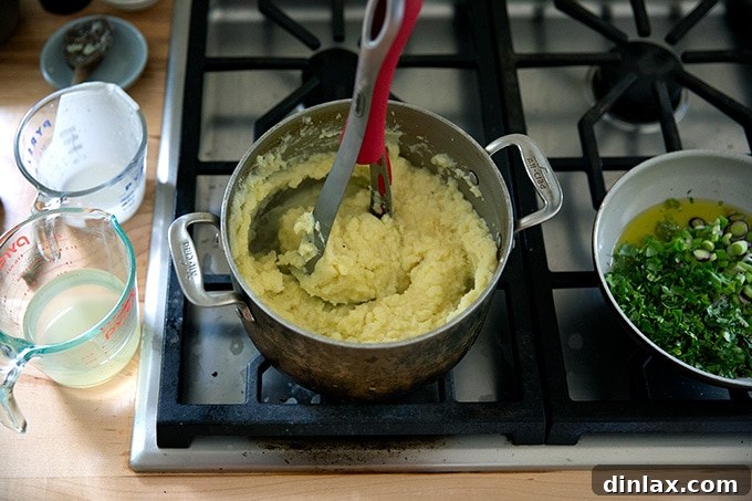 A potato masher actively mashing cooked potatoes in a pot with added liquids, aiming for a smooth consistency.