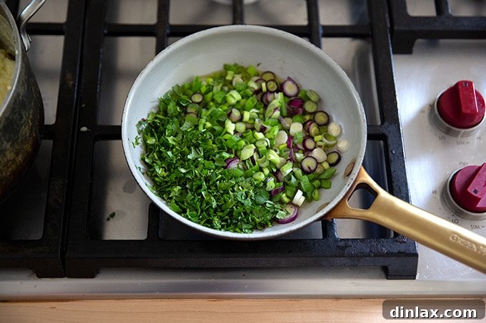 A small skillet on the stovetop with sliced scallions and chopped cilantro, drizzled with olive oil and red pepper flakes.