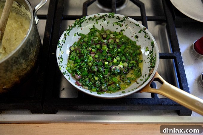 The scallions and cilantro in the skillet are visibly softened and sizzling gently in the olive oil, indicating they are cooked.