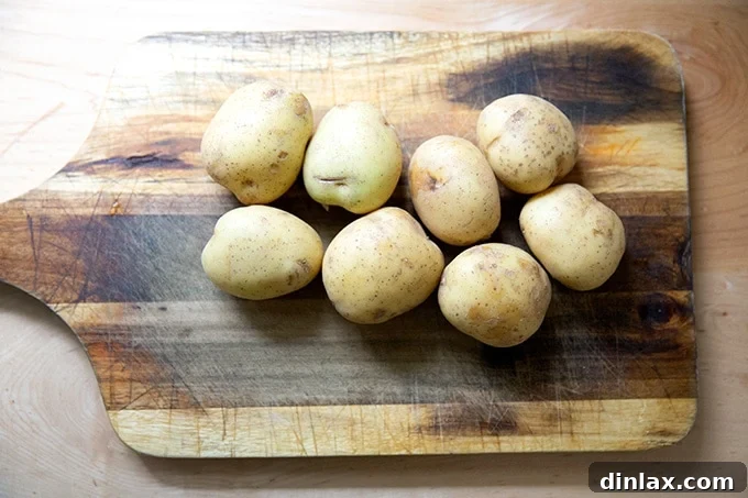 Fresh Yukon Gold potatoes on a wooden cutting board, ready for peeling and chopping.