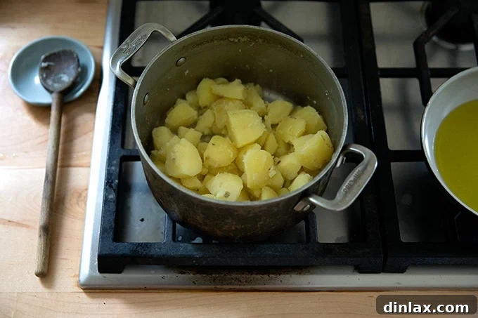 A pot of cooked, drained potatoes on the stovetop, gently steaming to dry out excess moisture.