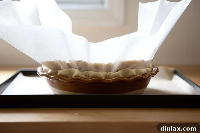 A pie plate fitted with a pie crust, lined with parchment paper and filled with pie weights.