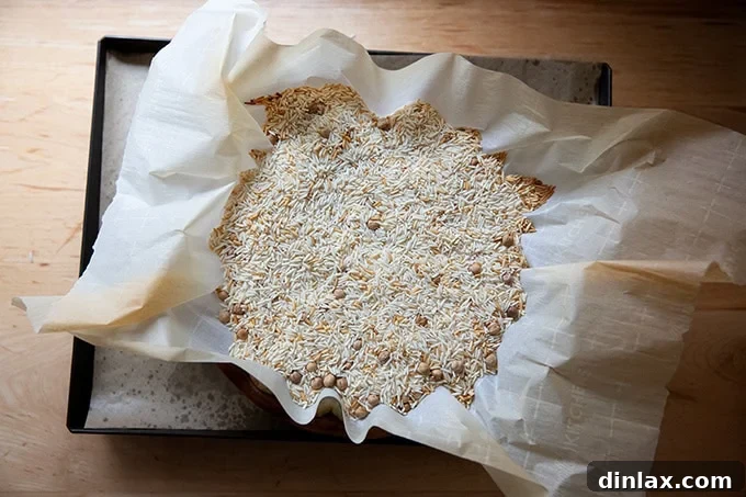 An overhead shot of pie weights — a mix of dried rice and chickpeas — filling a parchment-lined pie plate.