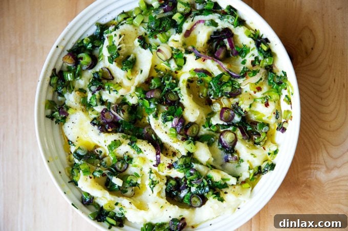 A serving bowl filled with creamy, herby mashed potatoes, garnished with fresh herbs.