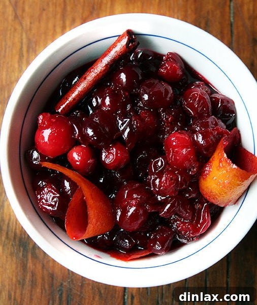 A vibrant red wine cranberry sauce in a serving bowl, garnished with fresh orange zest.