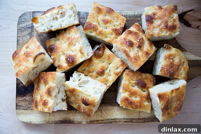 Freshly baked sourdough focaccia, cut into squares and garnished with herbs, on a wooden board.
