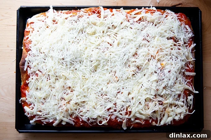 A Sicilian-style pizza crust topped with a rich layer of tomato sauce and abundant grated cheese.