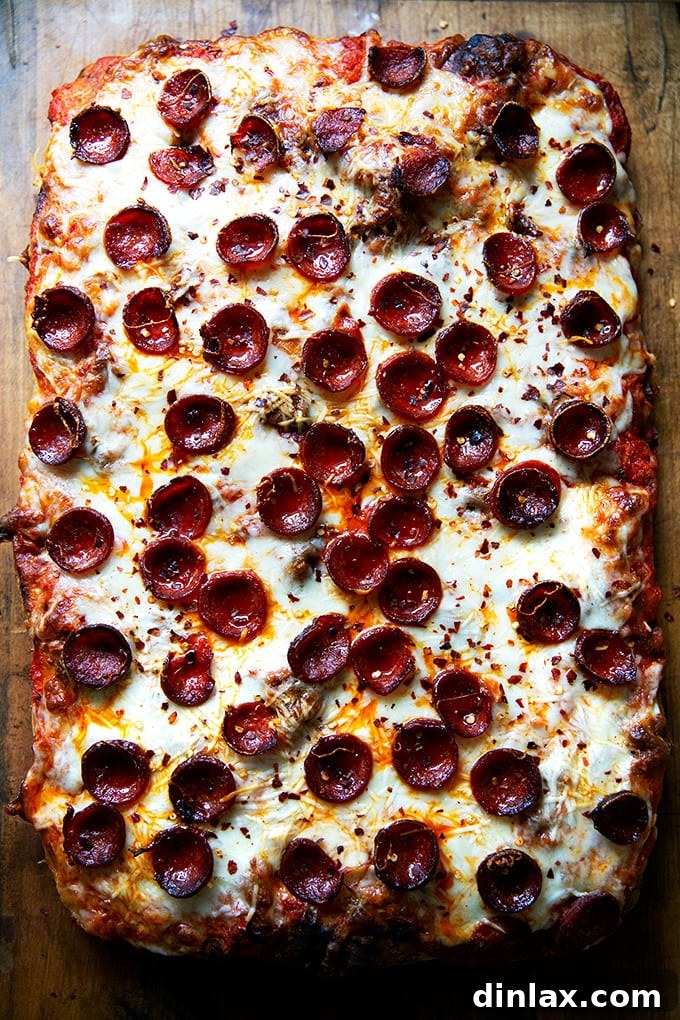 A close-up of a freshly baked Sicilian-style pepperoni pizza, adorned with a sprinkle of crushed red pepper flakes.