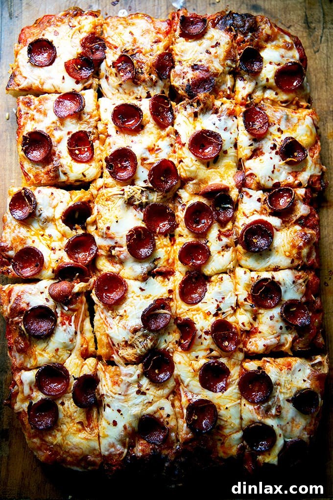A freshly baked Sicilian-style pepperoni pizza, neatly cut into squares on a wooden cutting board.