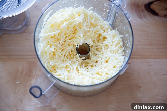 Perfectly grated cheddar cheese, glistening and ready for the next step, collected in the bowl of a food processor.