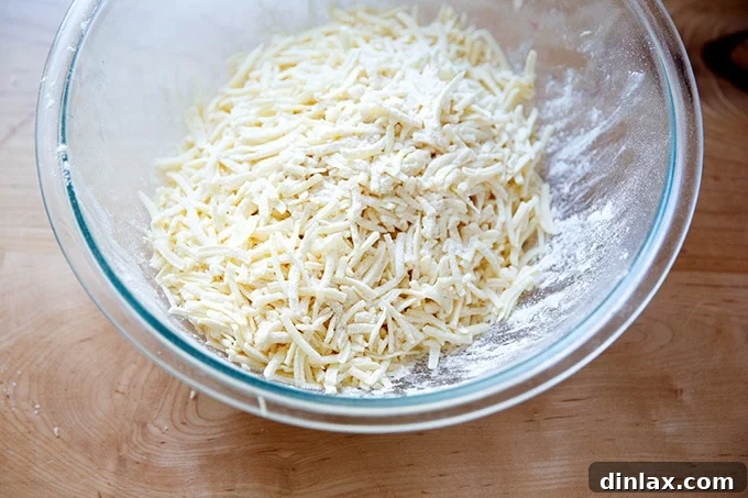 Grated cheddar cheese, lightly coated and tossed with flour in a bowl, prepared for the cheese sauce.