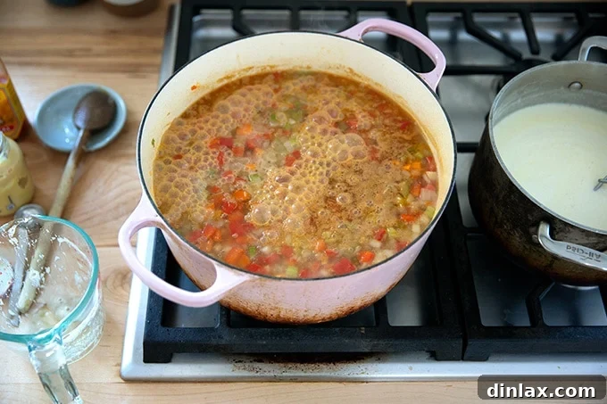A generous pour of beer being added to the large pot of simmering soup, infusing it with distinctive flavor.