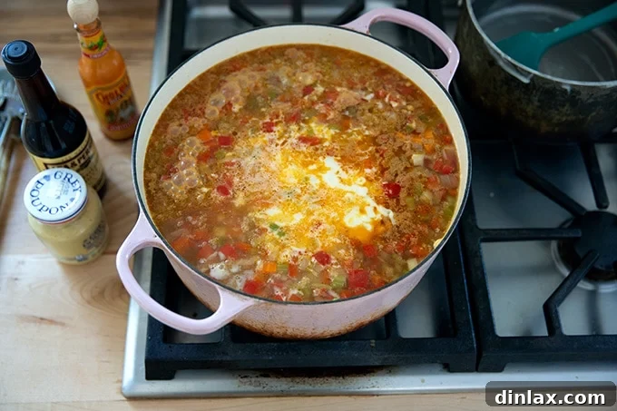 The creamy cheese sauce, mustard, Worcestershire, and hot sauce now combined with the simmering Vermont cheddar cheese soup in a large pot, creating a rich blend.