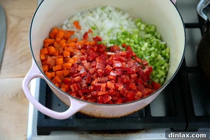Colorful diced vegetables, seasoned with salt, gently simmering in a large pot with olive oil, creating the aromatic base of the soup.