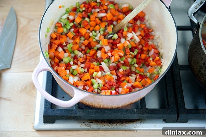 A large pot on the stovetop filled with a vibrant mix of sautéed vegetables, expertly stirred and softened.