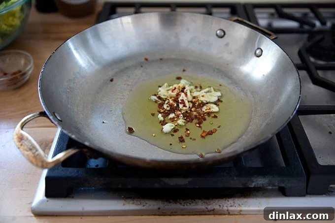 Vibrant Green Sauté 5 A large skillet stovetop with some olive oil, slice garlic, and crushed red pepper flakes inside.