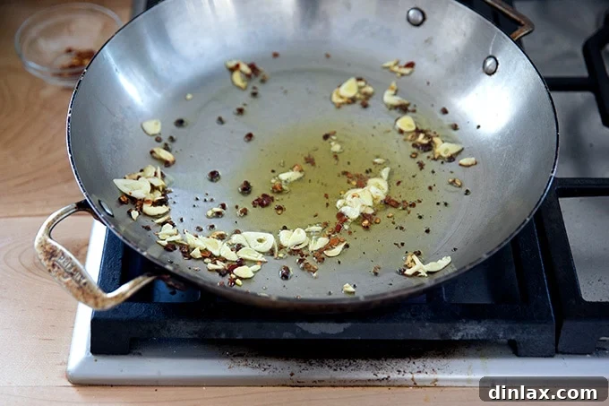 Vibrant Green Sauté 6 A large skillet stovetop with some olive oil, slice garlic, and crushed red pepper flakes inside.