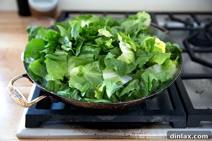 Vibrant Green Sauté 7 A large skillet stovetop with some olive oil, slice garlic, crushed red pepper flakes, and a heap of escarole inside.