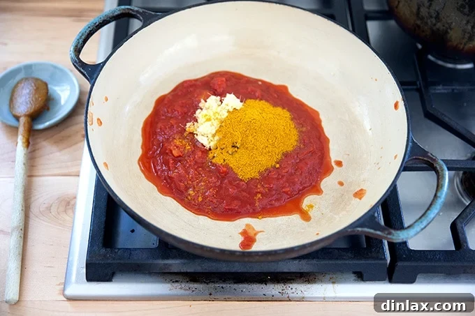 Effortless Butter Chicken and Chickpeas Instant Pot or Stovetop 19 A large braising pan on the stovetop filled with a vibrant mix of crushed tomatoes, curry powder, minced ginger, garlic, and salt.