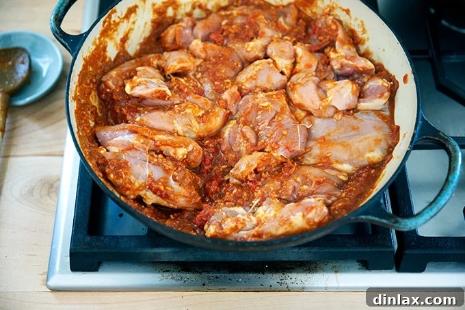 Effortless Butter Chicken and Chickpeas Instant Pot or Stovetop 20 A braiser on a stovetop, filled with raw chicken thighs coated in the butter chicken sauce ingredients, covered and ready to cook.