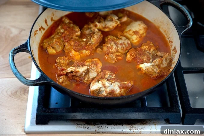 Effortless Butter Chicken and Chickpeas Instant Pot or Stovetop 21 A large braiser on the stovetop, containing fully cooked butter chicken, with the chicken pieces ready to be removed from the sauce.