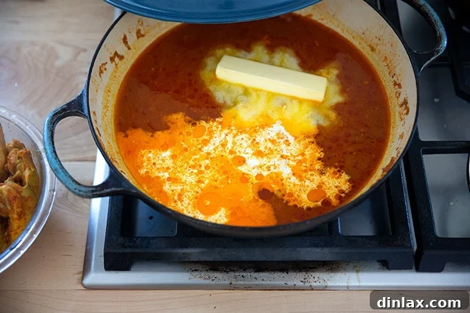 Effortless Butter Chicken and Chickpeas Instant Pot or Stovetop 22 A braiser on the stovetop, with butter chicken sauce, a stick of butter, and 1/4 cup heavy cream added, awaiting stirring.