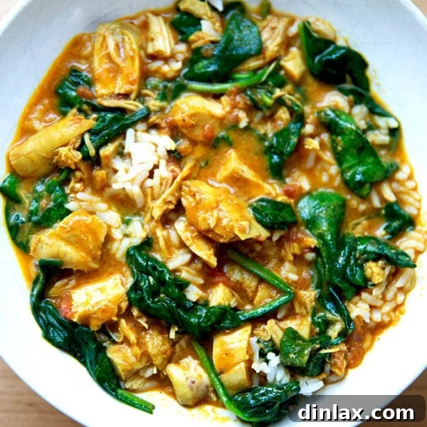 A bowl of butter chicken with spinach and rice.