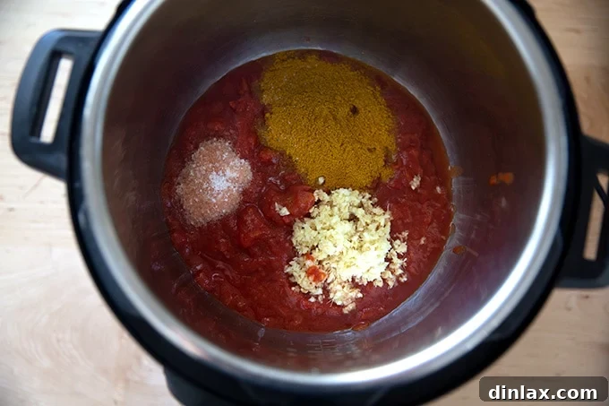 Effortless Butter Chicken and Chickpeas Instant Pot or Stovetop 6 The inner pot of an Instant Pot filled with crushed tomatoes, curry powder, minced ginger, garlic, and kosher salt.